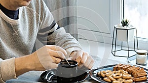 Man interferes with coffee in a cup. He is very sad. Home in his kitchen. He worries because of his problems.