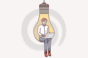 Man inventor with laptop sits in light bulb, symbolizing inspiration for coming up with ideas