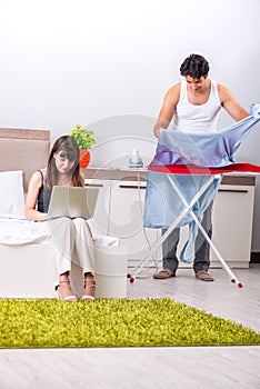 The man ironing, his lazy wife sitting