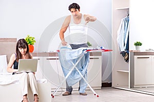 The man ironing, his lazy wife sitting