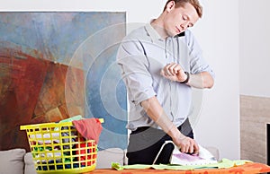 Man irons clothes and looks at his watch