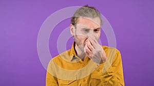 man on isolated purple background pinches his nose with his fingers. 4K