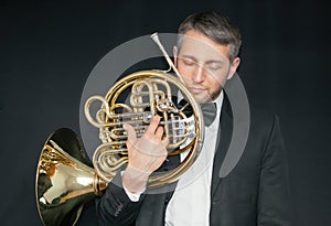 A man in a jacket on his naked body, holding a musical instrument. Waldhorn