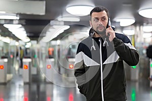 Man in jacket with a mobile phone near turnstile in subway