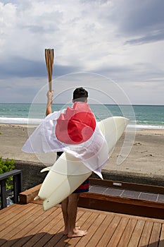 Man with Japanese flag , surfboard and torch used for sporting event.