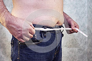 a man in jeans with a bare torso and a small belly with a measuring tape instead of a trouser belt close-up of the