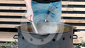 A man in jeans is cooking in a cast-iron cauldron in the open air. Stirring the ingredients in a boiling pan. The concept of a pic