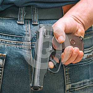 Man in jeans holding a gun behind his back