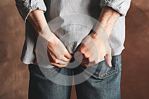 Man in jeans holds his ass on background. Hemorrhoids