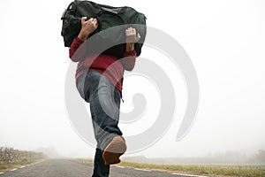 man in jeans and red mackintosh on foggy road with unrecognisable suitcase in tow