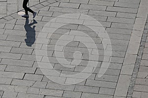 A man in jeans walks over a wide area, and on the side is his shadow.