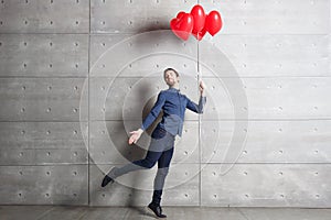 Man jumping indoors on background gray wall with red heart shaped balloons