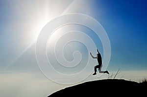 Man jumping on mountain peak at bright sky