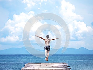 Man jumping off wooden bridge into blue sea.