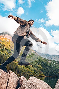 man jumping from rock at lake beach in mountains