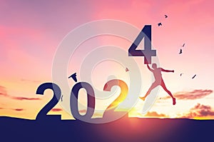 Man jumping on sunset sky with birds flying at top of mountain and number 2024 abstract background. Happy new year and holiday