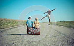 Man jumping and two children sitting on suitcase