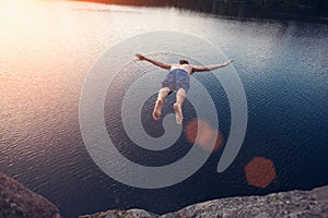 Man jumping into the water from cliff at sunset with outspread hands