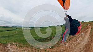Man jumps on a land to fly a glider in sky.