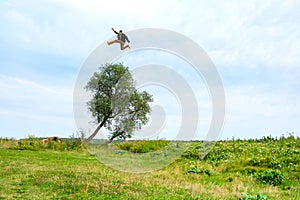 A man jumps over a tree growing on a field on a summer day