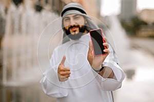 Man in kaffiyeh and thobe with a phone in hands photo