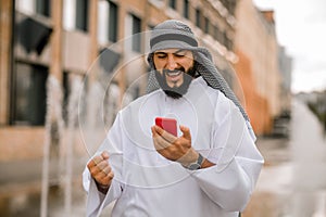 Man in kaffiyeh and thobe with a phone in hands photo