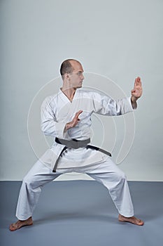 A man in karategi trains formal karate exercises on a gray cover