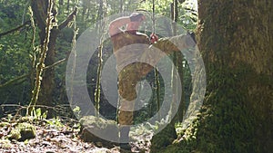 A man in khaki clothes trains in the forest, kicking a tree trunk with moss. Fight with a tree