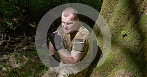 A man in a khaki uniform is resting in the forest under a tree