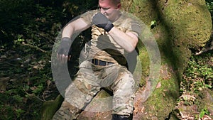 A man in a khaki uniform is resting in the forest under a tree