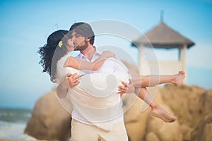Man kisses a beautiful woman, holding her in his arms, against the rocks, the sea and the sky