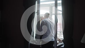 A man kisses a girl in black pajamas sitting on the window