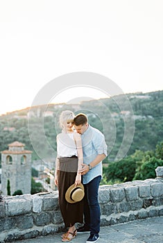 Man kisses a woman shoulder near a stone fence against a background of mountains