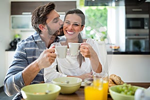 Man kissing on woman cheeks while having breakfast