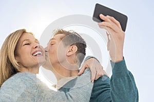 Man Kissing Woman While Taking Self Portrait On Cell Phone