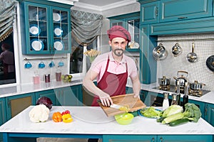 Man at kitchen cooking vegetable salad with paprika and mushrooms. Handsome chef cut orange pepper. Vegetables for healthy life