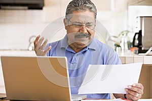 Man in kitchen with laptop and paperwork