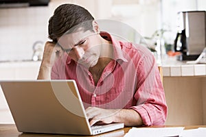 Man in kitchen using laptop frowning