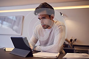 Man In Kitchen Working Or Studying From Home Using Digital Tablet