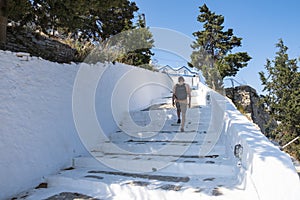 A Man with Knapsack Going Up a Set of White Steps Towards Symi Castle, Greece