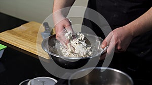 Man kneading dough with his hands in a metal bowl at the kitchen. Art. A cook preparing dough, mixing ingredients with