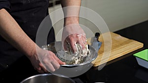 Man kneading dough with his hands in a metal bowl at the kitchen. Art. A cook preparing dough, mixing ingredients with
