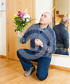 Man kneeling with bouquet of flowers.