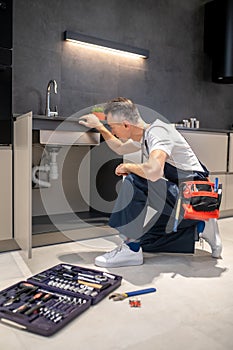 Man kneeling down touching sink inspecting pipes