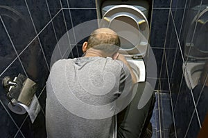 The man is kneeling and fixing the toilet in the home bathroom