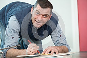 man kneeling on floor marking tile to cut