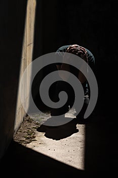 Man kneeling and holding his head with his hands, depressed and desperate in darkness with one sliver of light