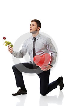 Man kneeling with red rose and heart balloon.