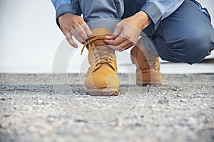 Man kneels down rope tie shoes industry boots for worker. Close up shot of man hands tied shoestring for his brown construction