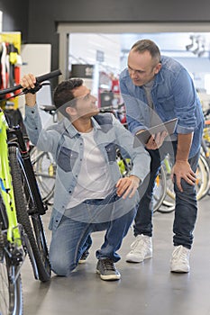 Man knelt by bicycle being shown tablet screen by second man